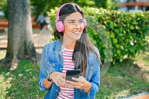 Young beautiful hispanic girl smiling happy using smartphone and headphones sitting at the park