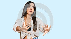 Young beautiful hispanic girl wearing casual clothes afraid and terrified with fear expression stop gesture with hands, shouting