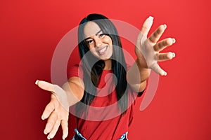 Young beautiful hispanic girl wearing casual red tshirt looking at the camera smiling with open arms for hug