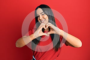 Young beautiful hispanic girl wearing casual red tshirt smiling in love doing heart symbol shape with hands