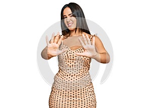 Young beautiful hispanic girl wearing sexy party dress afraid and terrified with fear expression stop gesture with hands, shouting