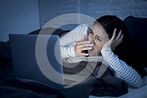 Young beautiful hispanic internet addict woman on bed with computer laptop yawning tired