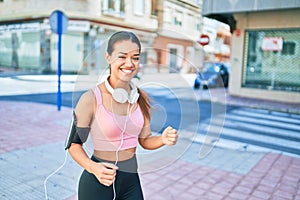 Young beautiful hispanic sport woman wearing runner outfit and headphones, smiling happy running at the town