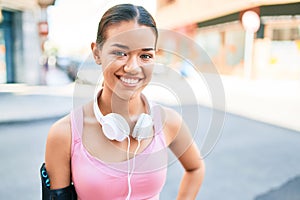 Young beautiful hispanic sport woman wearing runner outfit and headphones smiling happy at the town
