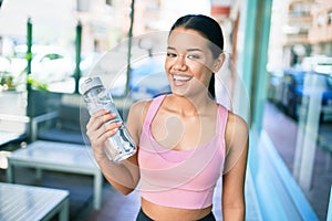 Young beautiful hispanic sporty woman wearing fitness outfit smiling happy and natural at the town drinking fresh water from the
