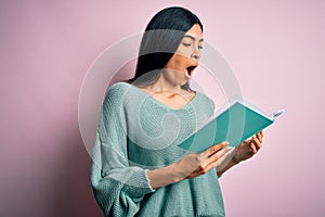 Young beautiful hispanic student woman reading a book over pink isolated background scared in shock with a surprise face, afraid