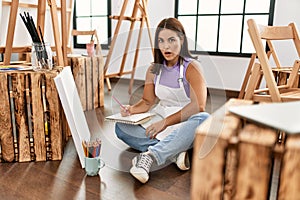 Young beautiful hispanic woman at art studio scared and amazed with open mouth for surprise, disbelief face