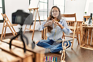 Young beautiful hispanic woman artist recording draw lesson communicate with deaf language at art studio