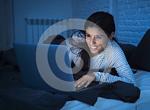 Young beautiful hispanic woman on bed at home laughing happy on laptop computer at night