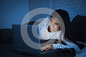 Young beautiful hispanic woman on bed at home laughing happy on laptop computer at night