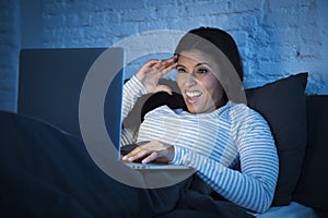 Young beautiful hispanic woman on bed at home laughing happy on laptop computer at night