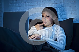 Young beautiful hispanic woman on bed at home working happy on laptop computer at night