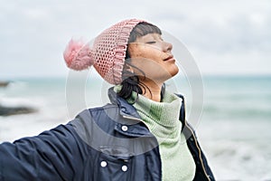 Young beautiful hispanic woman breathing with arms open at seaside