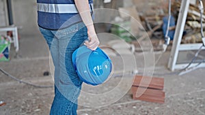 Young beautiful hispanic woman builder holding hardhat walking at construction site