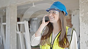 Young beautiful hispanic woman builder smiling confident talking on smartphone at construction site