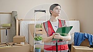 Young beautiful hispanic woman builder writing on clipboard at new home