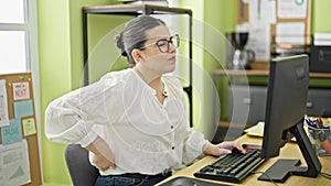 Young beautiful hispanic woman business worker sitting on the table suffering for backache at the office