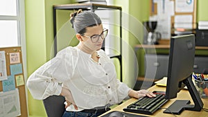 Young beautiful hispanic woman business worker sitting on the table suffering for backache at the office
