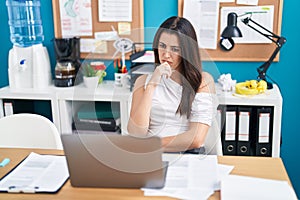 Young beautiful hispanic woman business worker using laptop with doubt expression at office