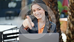 Young beautiful hispanic woman business worker using laptop pointing to camera at coffee shop terrace