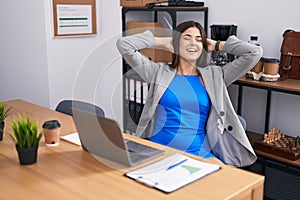 Young beautiful hispanic woman business worker using laptop relaxed with hands on head at office