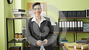 Young beautiful hispanic woman business worker using smartphone smiling at office