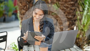 Young beautiful hispanic woman business worker using touchpad and laptop sitting on table at park