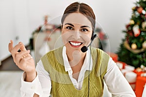 Young beautiful hispanic woman call center agent sitting by christmas tree speaking at home