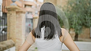 A young, beautiful hispanic woman caught in a casual, outdoor portrait, standing backward in a green city park, her back view