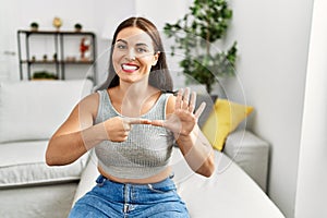 Young beautiful hispanic woman communicate with deaf language sitting on sofa at home