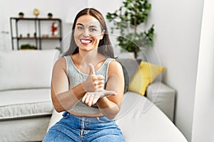 Young beautiful hispanic woman communicate with deaf language sitting on sofa at home