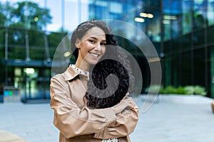 Young beautiful hispanic woman with curly hair outside office building, company worker smiling and looking at camera