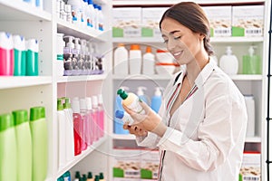 Young beautiful hispanic woman customer smiling confident holding shampoo bottles at pharmacy