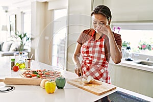 Young beautiful hispanic woman cutting onion crying at the kitchen