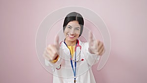 Young beautiful hispanic woman doctor doing thumbs up over isolated pink background