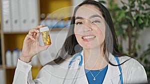Young beautiful hispanic woman doctor holding bottle of pills at the clinic