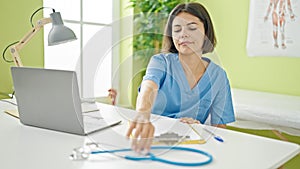 Young beautiful hispanic woman doctor using laptop holding stethoscope at clinic