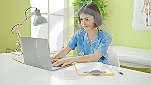 Young beautiful hispanic woman doctor using laptop wearing stethoscope at clinic