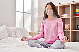 Young beautiful hispanic woman doing yoga exercise sitting on bed at bedroom