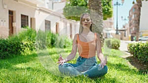 Young beautiful hispanic woman doing yoga exercise sitting on floor at park