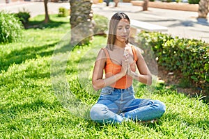 Young beautiful hispanic woman doing yoga exercise sitting on floor at park