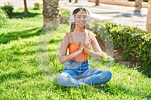 Young beautiful hispanic woman doing yoga exercise using headphones at park