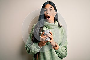 Young beautiful hispanic woman drinking a cup of hot coffee over isolated background scared in shock with a surprise face, afraid