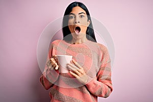 Young beautiful hispanic woman drinking a cup of hot coffee over pink isolated background scared in shock with a surprise face,