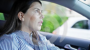 Young beautiful hispanic woman driving a car speaking to the passenger on the road