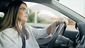 Young beautiful hispanic woman driving a car wearing glasses on the road