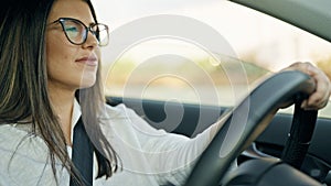 Young beautiful hispanic woman driving a car wearing glasses on the road