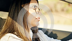 Young beautiful hispanic woman driving a car wearing glasses on the road