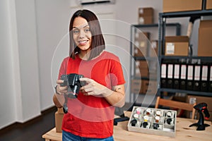 Young beautiful hispanic woman ecommerce business worker smiling confident holding professional camera at office