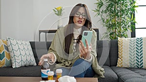 Young beautiful hispanic woman having medical video call consultation showing medicine bottle at home